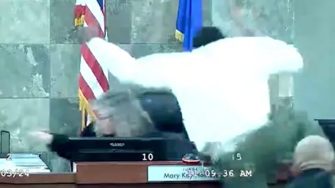 A man leaps on top of a judge in a courtroom.