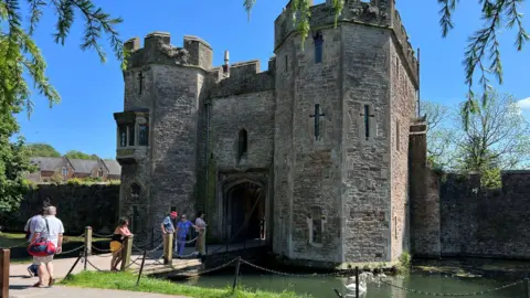 BBC The Bishop's Palace in Wells seen from the outside with people standing on the drawbridge