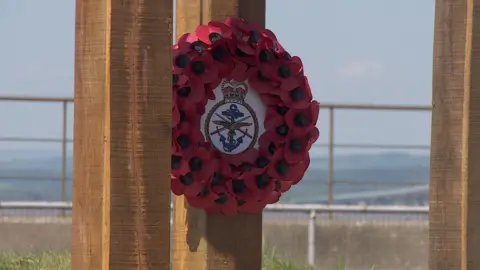 Three wooden pillars with a poppy display. The sea can be seen in the background.
