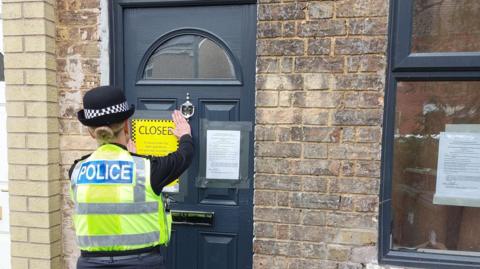 Police officer placing closure notice on front door