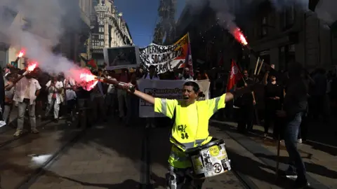 EPA A woman in bright neon clothing carries flares as a crowd walks behind her