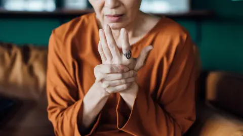 Getty Images A woman is seen holding her hand in pain. She is wearing an orange top. 