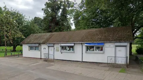 Google A white library building with a green space and trees
