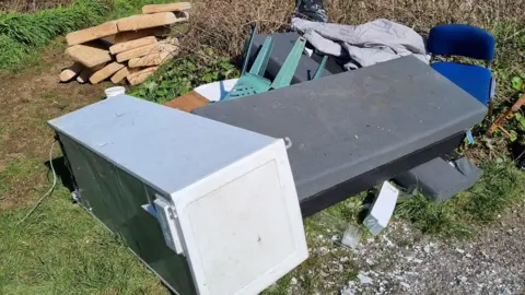 Cornwall Council A pile of fly-tipped rubbish at Conce Moor in Cornwall. A fridge, mattress, sofa cushions and chairs are piled on top of each other in the countryside