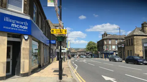 Aisha Iqbal/BBC A town centre high street. A yellow sign points to the Five Rise Quarter, identifying the town as Bingley. Shops line the street and there's light to busy traffic and pedestrian activity.