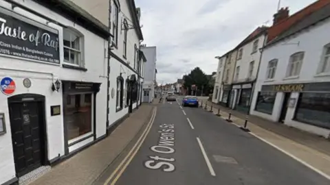 A Google street view image with white properties on both sides of the road. The left side building has a black sign that reads Taste of Raj and the right side property has a gold sign that reads Jalsagor. The picture is a file image and not related to the arrests.