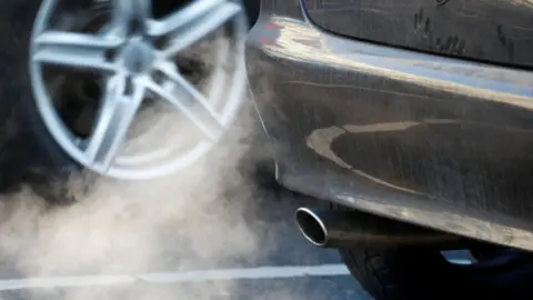 The picture shows a plume of white fumes coming out of a car's exhaust pipe