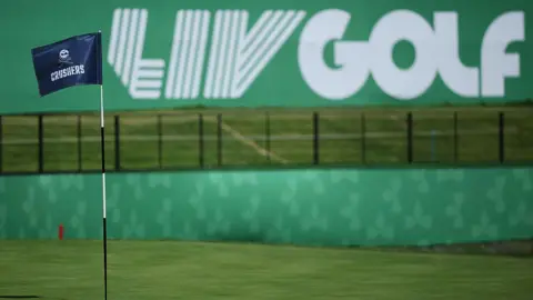 A flag on a golf course green in front of a sign that says 'LIV Golf'