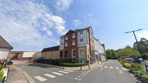 A Google photo of a Travelodge hotel with three floors next to a car park. No cars or people can be seen.