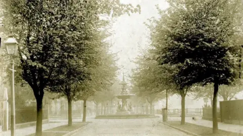 Carnegie Heritage Centre A sepia photograph of a tree-lined road with an ornate fountain in the middle