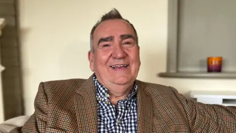 Deputy Simon Vermeulen - A man with a brown and red checked jacket, with a black and white checked shirt. 