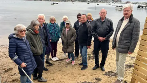 BBC The group of residents who are against the fence stood next to it and on the beach near the water.