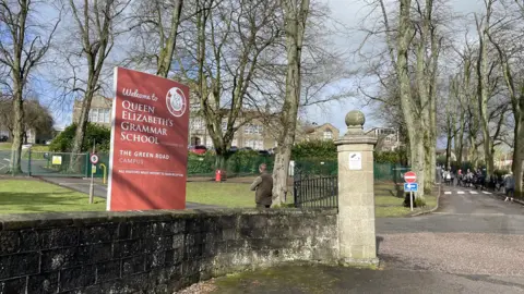 An external view of Queen Elizabeth's Grammar School in Ashbourne from the gates which includes a red sign.