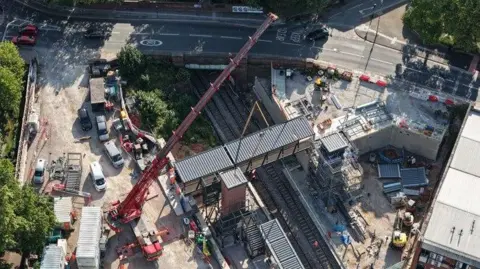 An aerial shot of a large crane placing a footbridge above a train track