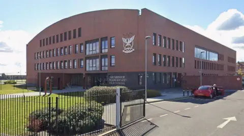 Google A modern brown brick building set behind a black gate with Archbishop Blanch CofE High School signage.