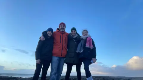 Sion Tudur Beti and her family stand on a mountain peak. They are all wrapped in warm clothing