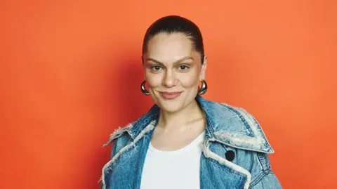 Jessie J with her hair tied back, big silver hoop earrings and a denim jacket and white top