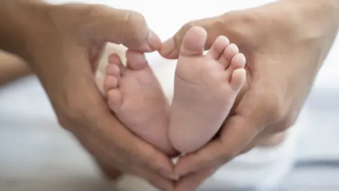 woman's hands cupping a baby's feet, producing a heart shape