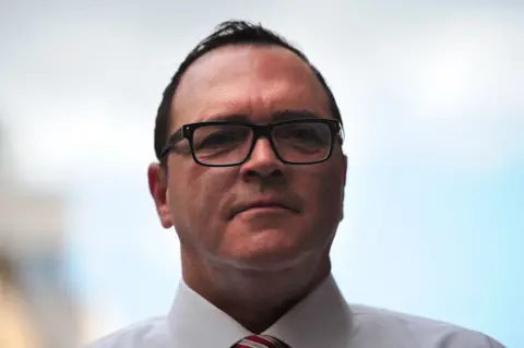 Getty Images Christopher Ciccone pictured in 2012 with short black hair, black glasses, and a white shirt with a red and grey striped tie