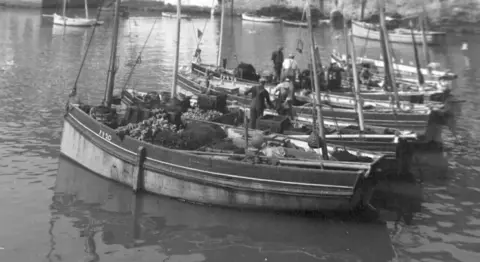 John Collings Black and white image of five Polperro Gaffers in the harbour with sailors on board. 