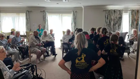 George Carden/BBC Residents in chairs and wheelchairs watching children dancing 