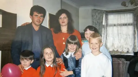 Family photo An old family photo of the Durakus, with two children in school uniforms and others in civilian clothes. The parents have their arms around them. 