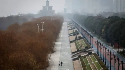 Getty Images Two people walk down an empty street in Wuhan, 27 January 2020