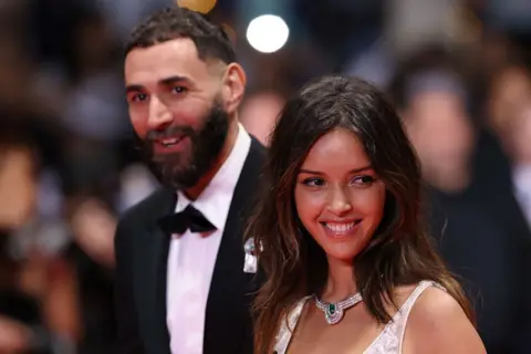 SAMEER AL-DOUMY / AFP / GETTY IMAGES A man and a woman smile as they walk down a red carpet and pose for photographers.