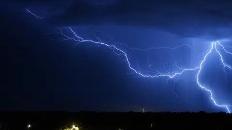 Ben A Blue forks of lightning strike during the night over a suburb.