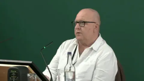 The Nottingham Inquiry Gary Carter, former mental health nurse, giving evidence at the Nottingham Inquiry. Gary is a middle-aged, bald, white man wearing a white shirt and glasses with a black frame. 
