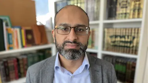 Photo shows Dr Sohail Hanif, chief executive of the National Zakat Foundation, standing in front of books