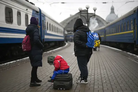 Getty Images Evacuees and a child, sitting on top of a suitcase, wait for a train to Romania, at the Lviv train station, western Ukraine, on March 5, 2022.