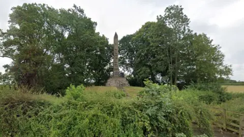 Google Stone obelisk with pointed top surrounded by trees