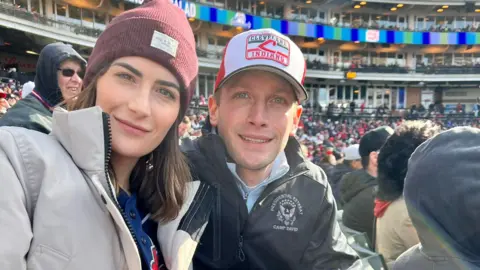 Max Miller / X Emily Moreno and Max Miller pose for a photo together at a sports game