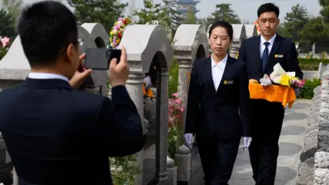 Getty Images Staff film a tomb sweeping ceremony for a customer