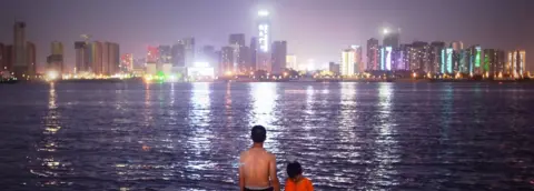 WANG ZHAO A man and child stand looking at the Wuhan skyline on the Yangtze River