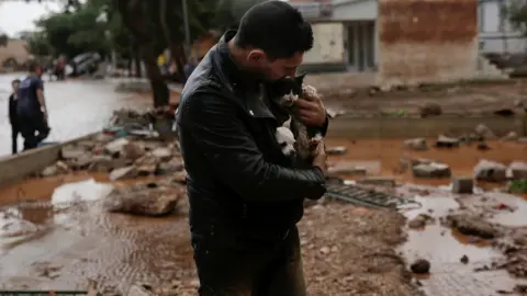 Reuters A local, carrying a dog in his jacket, holds a cat he saved from a tree
