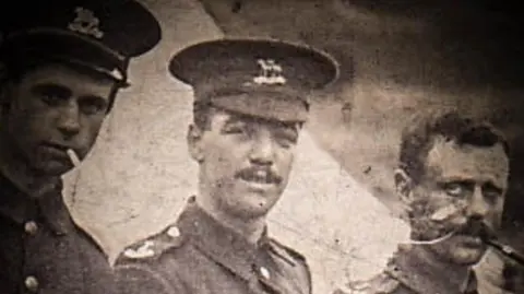 Rupert Thompson (centre) pictured early in his Army career. It is a grainy black and white image showing three soldiers. One on the left is smoking a cigarette and the man on the right has a pipe. Thompson is wearing his Army uniform, including a cap, and he has a moustache