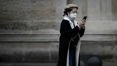 AFP/Getty Woman in a mask check her phone, Paris, 31 January 2020