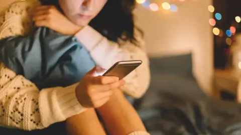 Getty Images Girl sits and holds phone