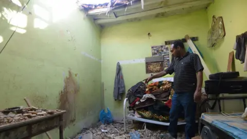 AFP A man shows the damage caused to a home in Riyadh that was hit by a piece of shrapnel from a ballistic missile fired by Yemeni Houthi rebels (26 March 2018)