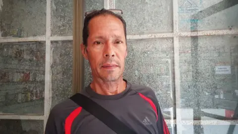 Carlos Herrera Mendieta Murillo stands in front of a shop