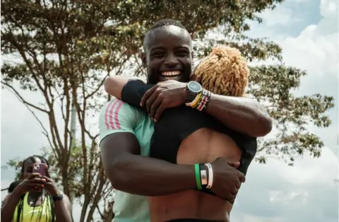 AFP Ferdinand Omanyala embraces his wife and fellow sprinter Laventa Omanyala. He is smiling from ear to ear in a green top.