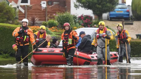 PA Media Residents are taken to safety in an inflatable boat by rescue workers in Wainfleet