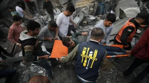 EPA-EFE/REX/Shutterstock Palestinians recover a wounded person from the rubble of a destroyed house following Israeli airstrikes, in Deir Al Balah, central Gaza Strip, 8 December 2023