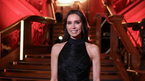Press Eye Christine Lampard is standing in front of the Titanic staircase. She is wearing a black halterneck dress and has dark hair. She is smiling at the camera