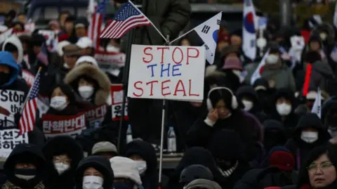 Pendukung Reuters Yoon memegang spanduk pembacaan "Hentikan pencurian itu"serta bendera Korea Selatan dan AS