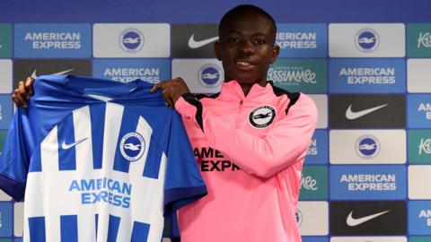Malick Yalcouye holds up a Brighton shirt after his move to the club