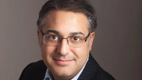A photo of Mr Jabbar, who is wearing a suit and glasses