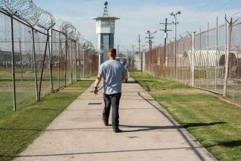 Getty Iamges/Giles Clarke A prisoner walks through a fenced section toward a guard tower at Louisiana State Penitentiary, also known as Angola